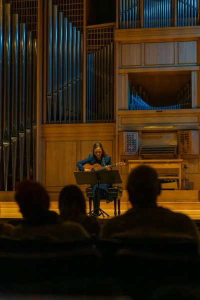 A women dressed in a blue suit plays guitar.