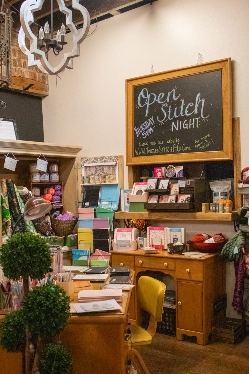 Materials available for purchase sit on a shelf underneath a sign advertising "Open Stitch Night" at the Twisted Stitch Nov. 22. 