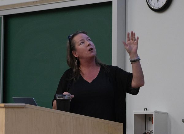 A woman in a black shirt with glasses on her head, looks up with her hand pointing above her.
