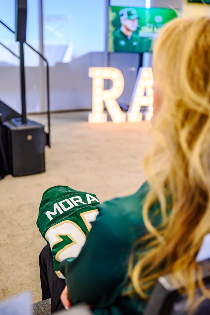 Kathy Mora sits in the front row of a Colorado State University press conference with a jersey for her husband, head football coach Jim Mora Dec. 1.