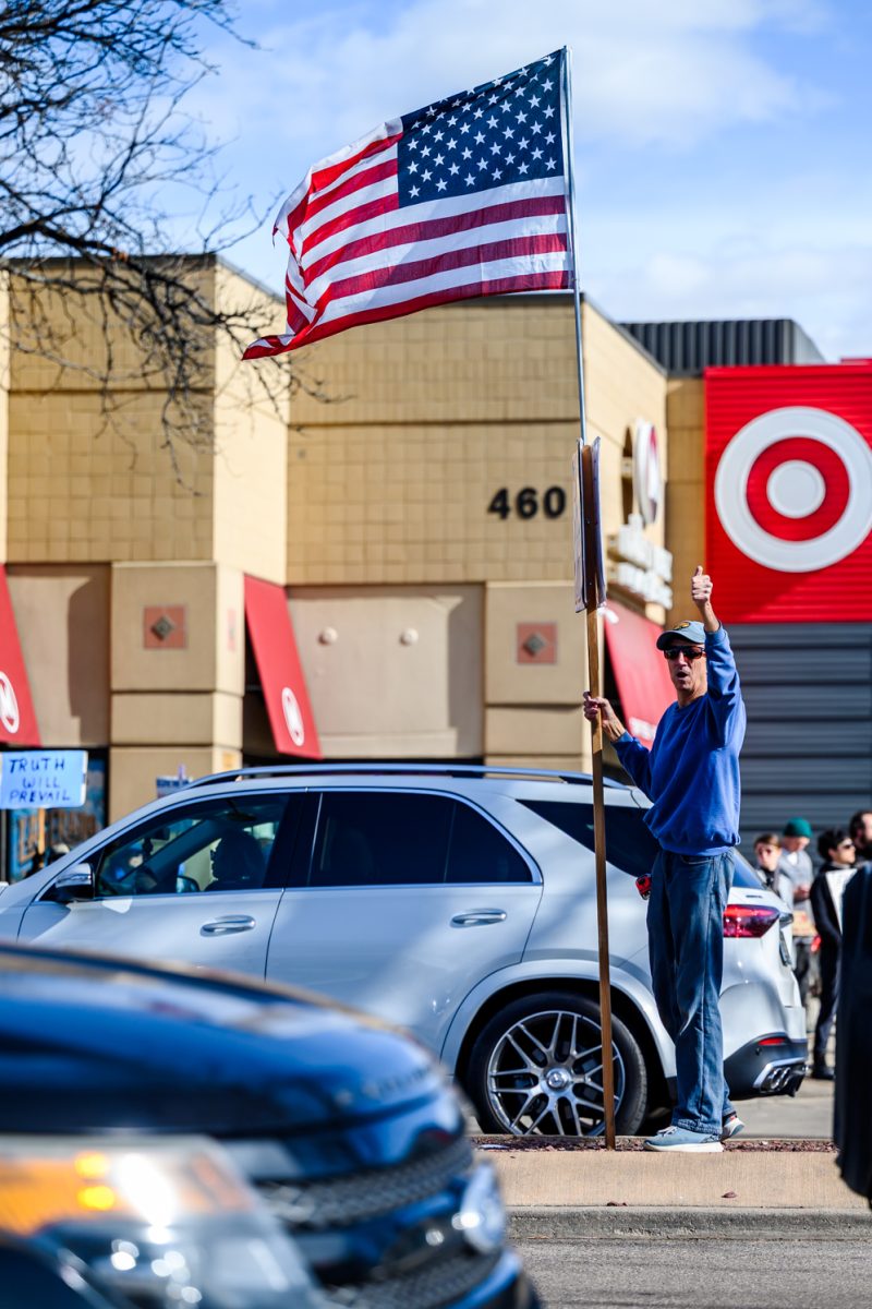A protester holding an American flag waves at passing cars during an anti-ICE strike on College Avenue and Mulberry Street Jan. 30.