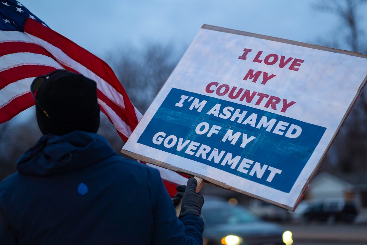 A man who requested to remain anonymous holds a sign and an American flag up for passing cars to see during a walk-out Tuesday, Jan. 20 protesting federal policies and ICE activities across the country. Participants gathered along College Avenue just north of Drake Road. 
