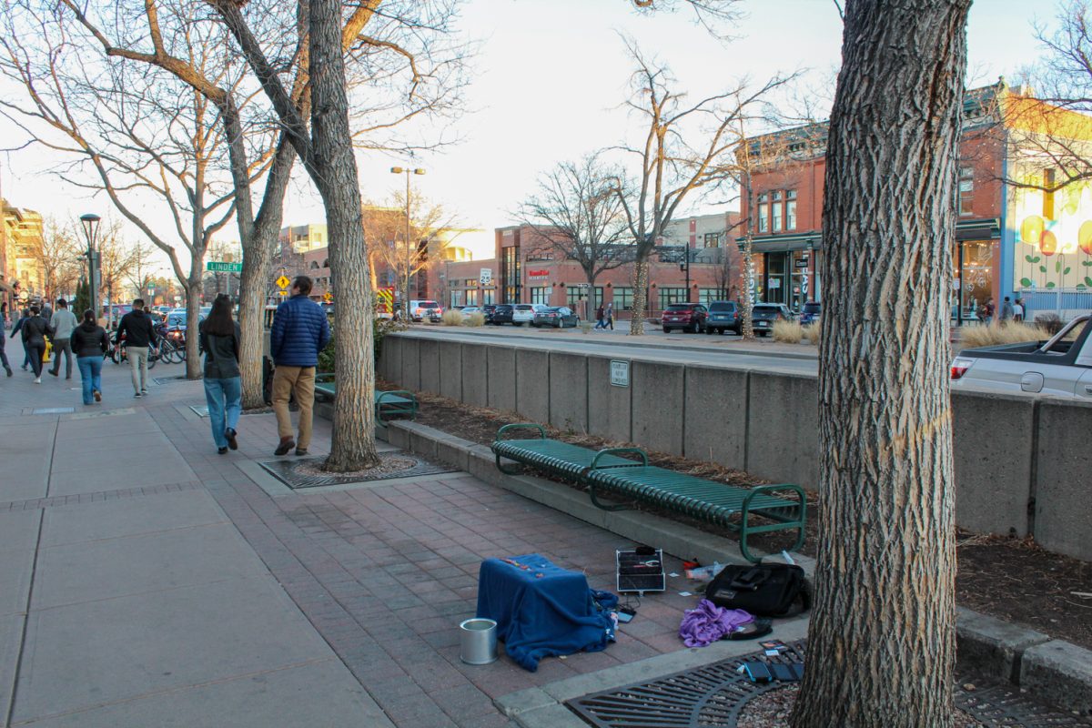 A variety of items sit on a sidewalk and people walk by.