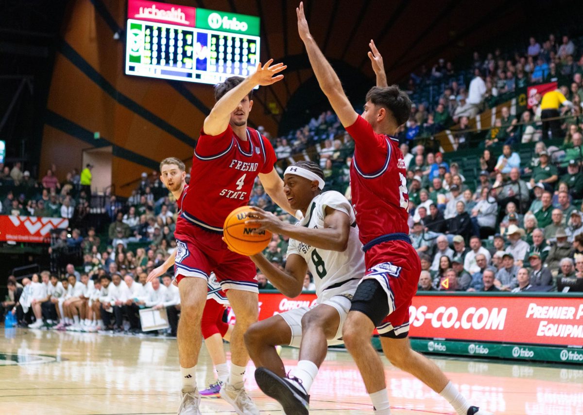 A man wearing an all white jersey and a white headband runs through two men wearing red jerseys on both sides of him.