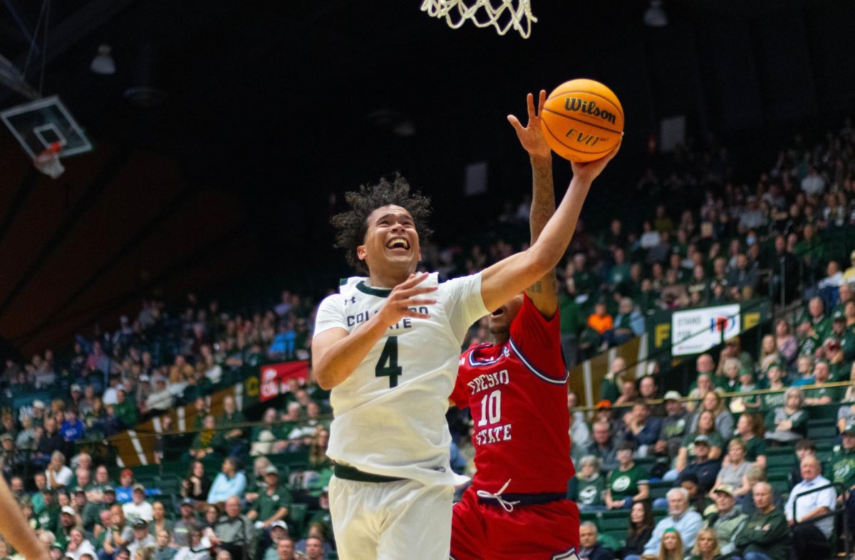 A man wearing an all white jersey extends his left hand up toward the basket as a man in an all red jersey tries to block the ball.