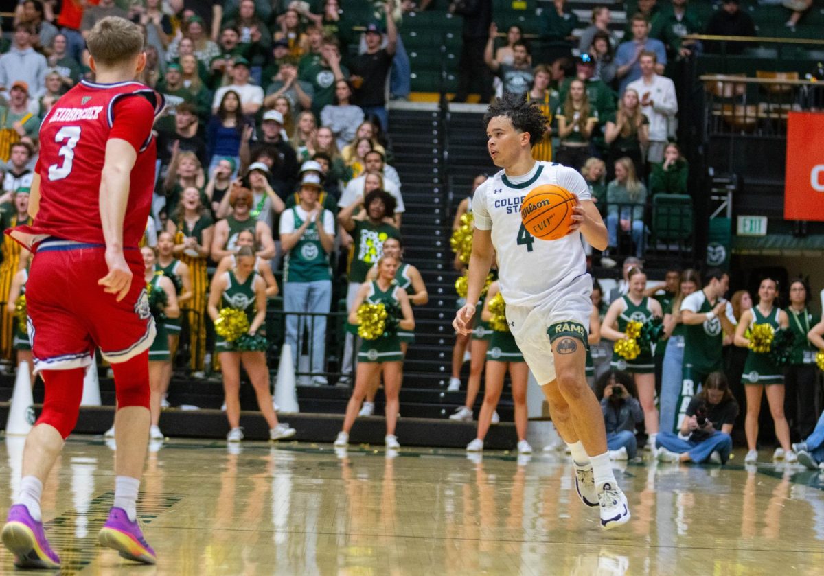 A man in an all white jersey has the ball in his left hand as he runs up the court. There is an man in an all red jersey in front of him.