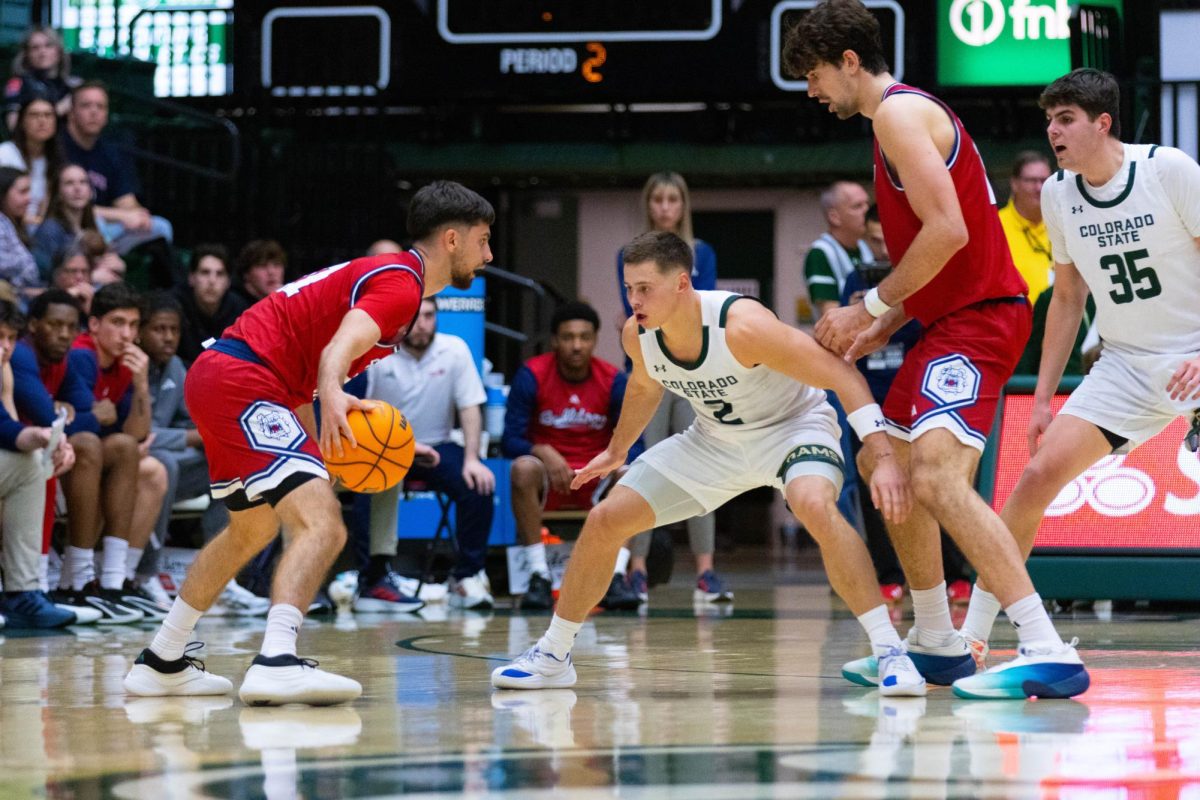 A man in an all red jersey dribbles the ball with his right hand as a man in an all white jersey is in a squat in front of him.