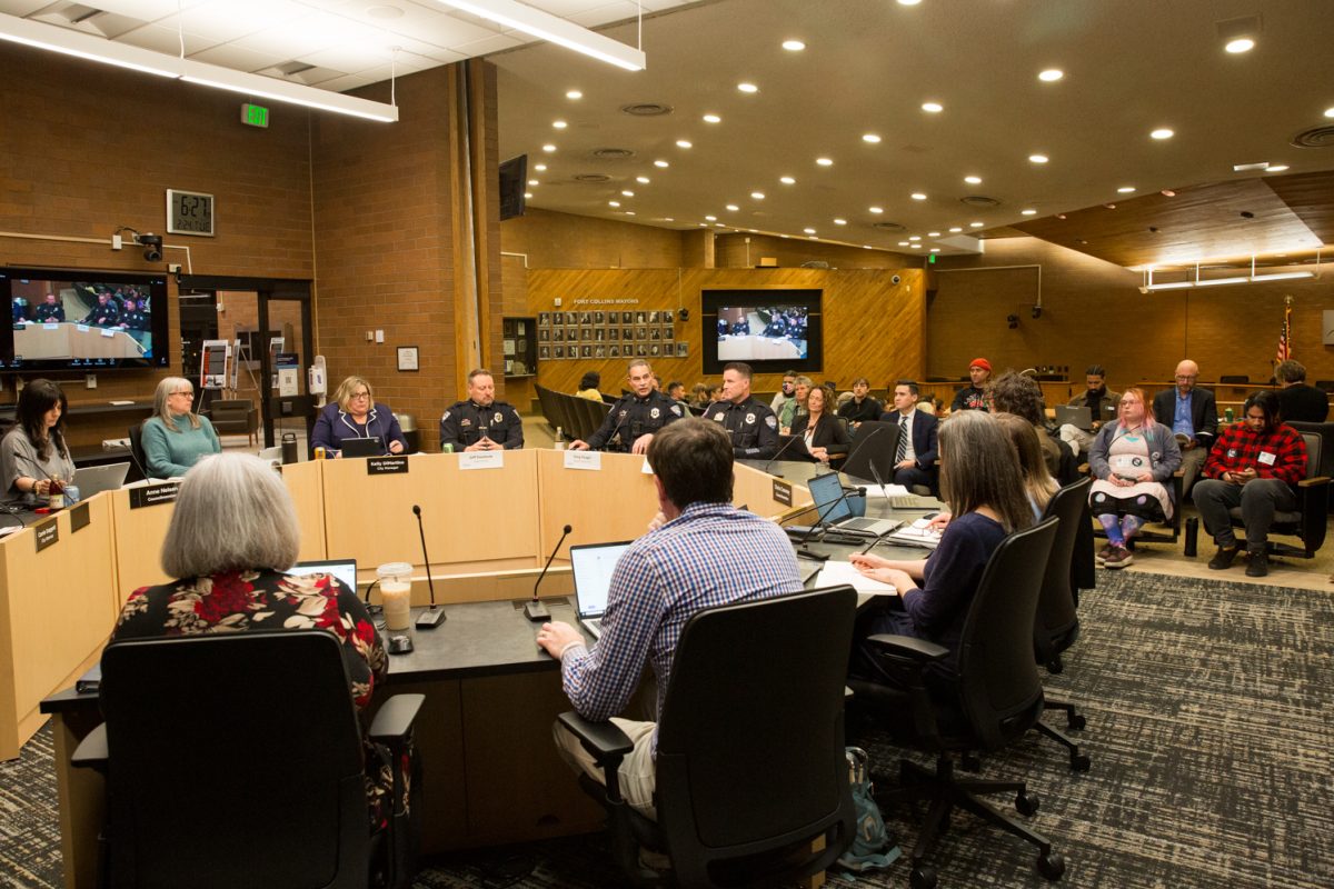 A large circular table with people sitting around it in chairs and people sitting in chairs behind it.