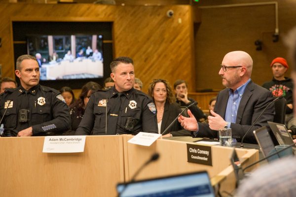 Two men in police uniforms listen to a man in a suit talk.