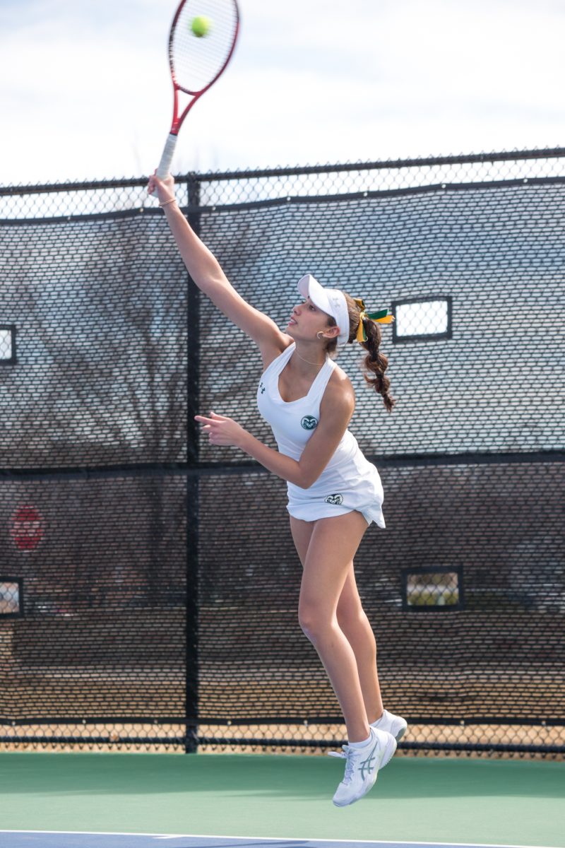 A girl in white with a racket reaches for a ball.