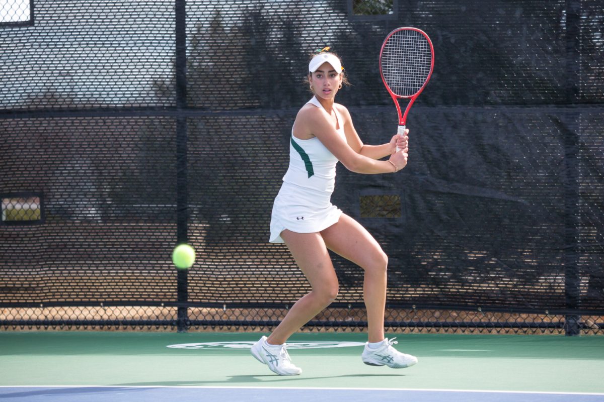 A girl in white with a racket reaches for a ball.