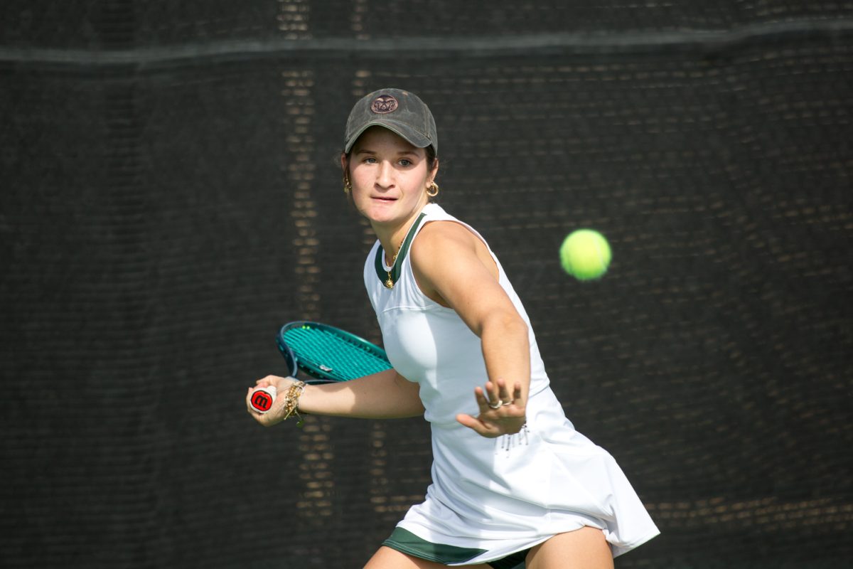 A girl in white with a racket reaches for a ball.