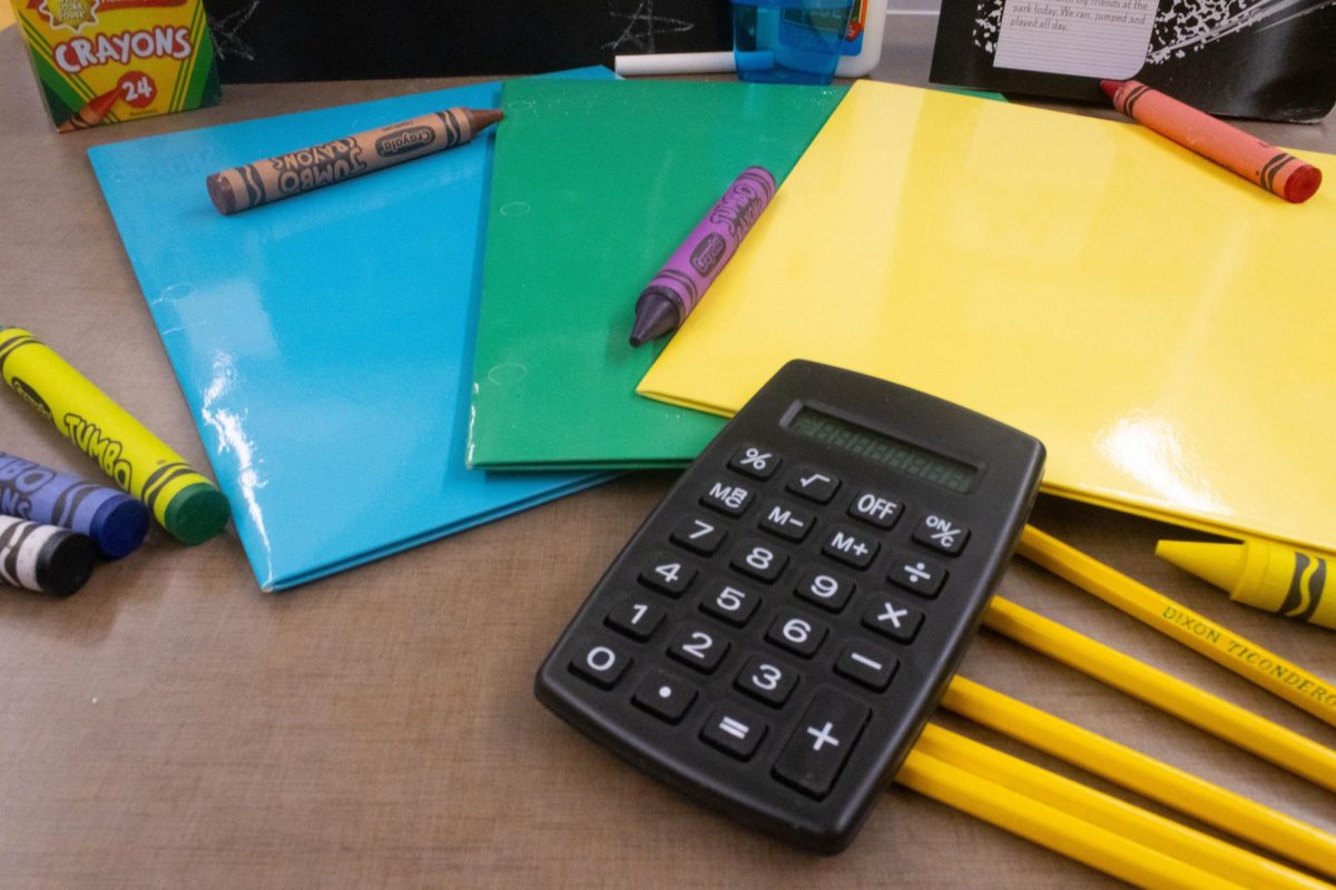 A black mini calculator lies on top of yellow pencils, as well as three different colored folders: blue, green, and yellow.