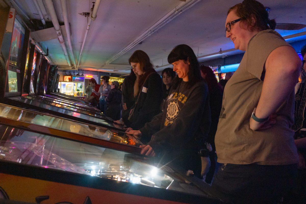 Emily Nicholson plays pinball as others watch during the Women, Trans, Femme league at Pinball Jones Feb 12. Erika Stonebay, who helped establish the league, said the league's goal is to create a space for women, trans, and femme-identifying players in the world of pinball, which is a male-dominated sport.