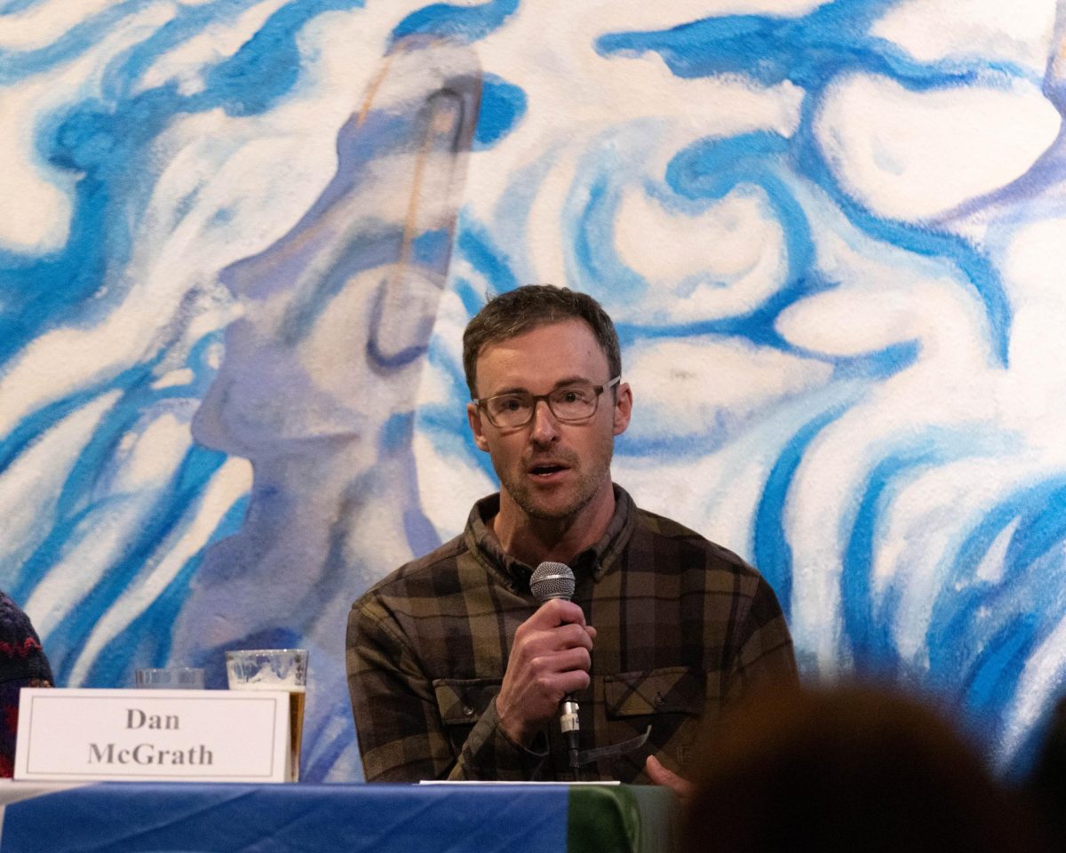 A man holds a microphone in front of his face while talking into it. He is wearing glasses.