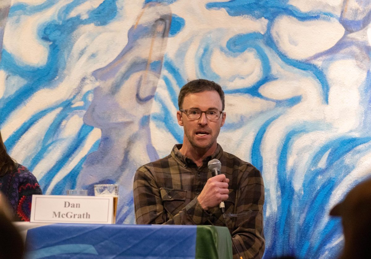 A man holds a microphone in front of his face as he talks into it. He is wearing glasses.