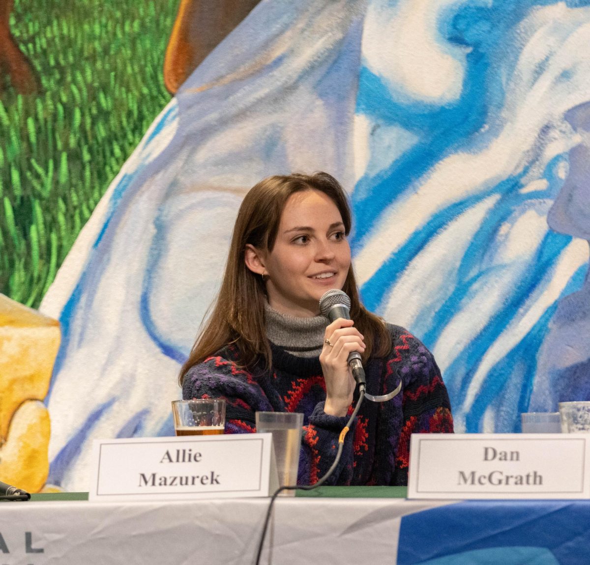 A woman holds a microphone in front of her face, she is smiling while talking into it.