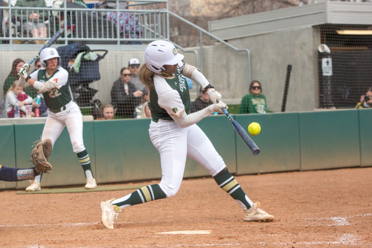 A girl in a green and white softball uniform swings a bat at a ball.