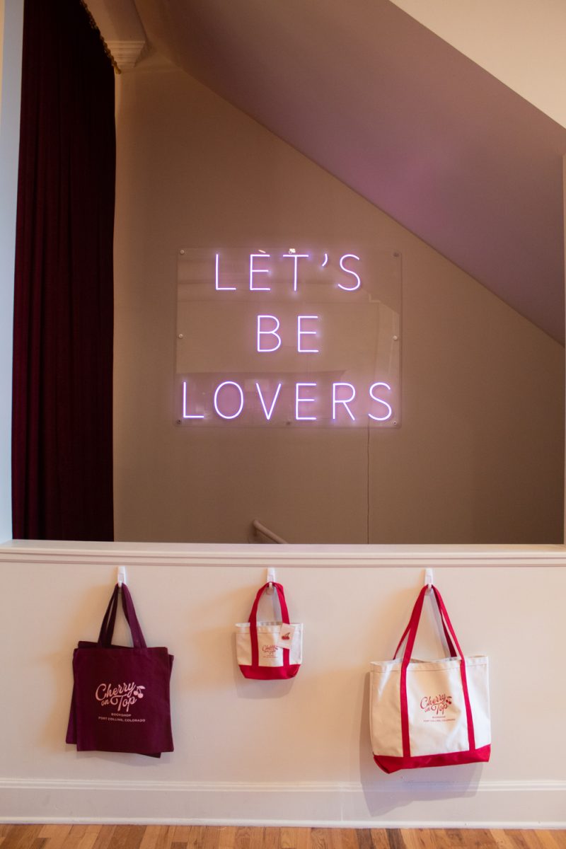 Merchandise hangs on a wall in front of a neon sign, inside Cherry On Top Bookshop in Downtown Fort Collins Mar. 5. Fort Collins’ first romance-only bookshop, Cherry On Top opened on February 13th of this year. The date was on theme - “Galentines day!” co-owner Meredith Glover said.