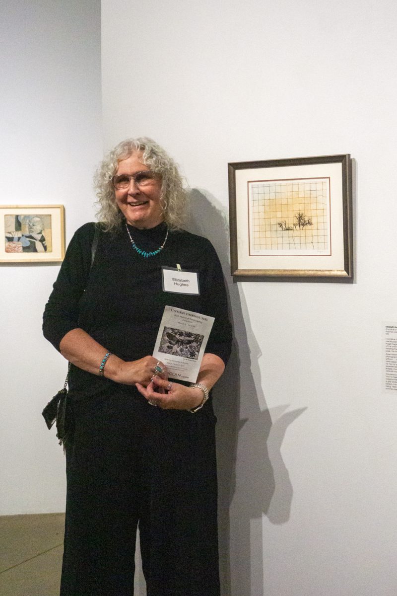 Artist Elizabeth Hughes stands next to her artwork on display at  "Under Pressure", part of the 2026 National Printmaking Exhibition at the Lincoln Center March 7. Hughes' art piece is a polymer plate photo etching, inspired by Davinci's "Copse of Trees."