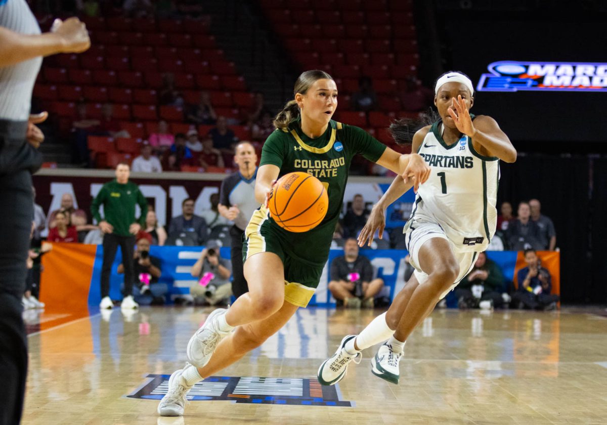 A woman in an all green jersey runs past a woman in an all white jersey, she has the ball in her right hand.