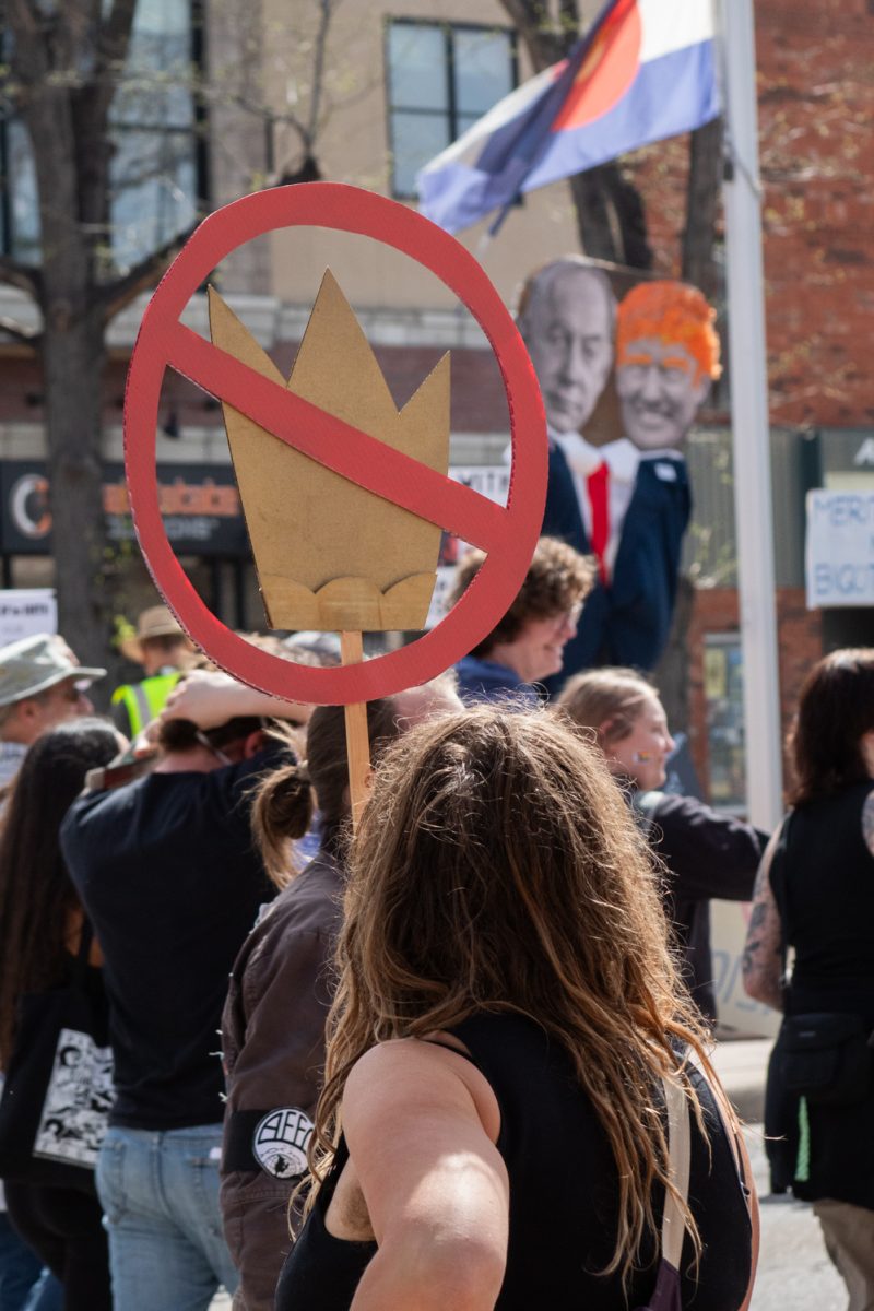 A No Kings protester raises their sign while standing on North College Avenue and cheering for marching protesters March 28. As part of the third No Kings rally, about 10,000 attendees marched through Fort Collins protesting the actions of the Trump Administration. “When immigrant rights are under attack, what do we do? Stand up, fight back!” protesters chanted.