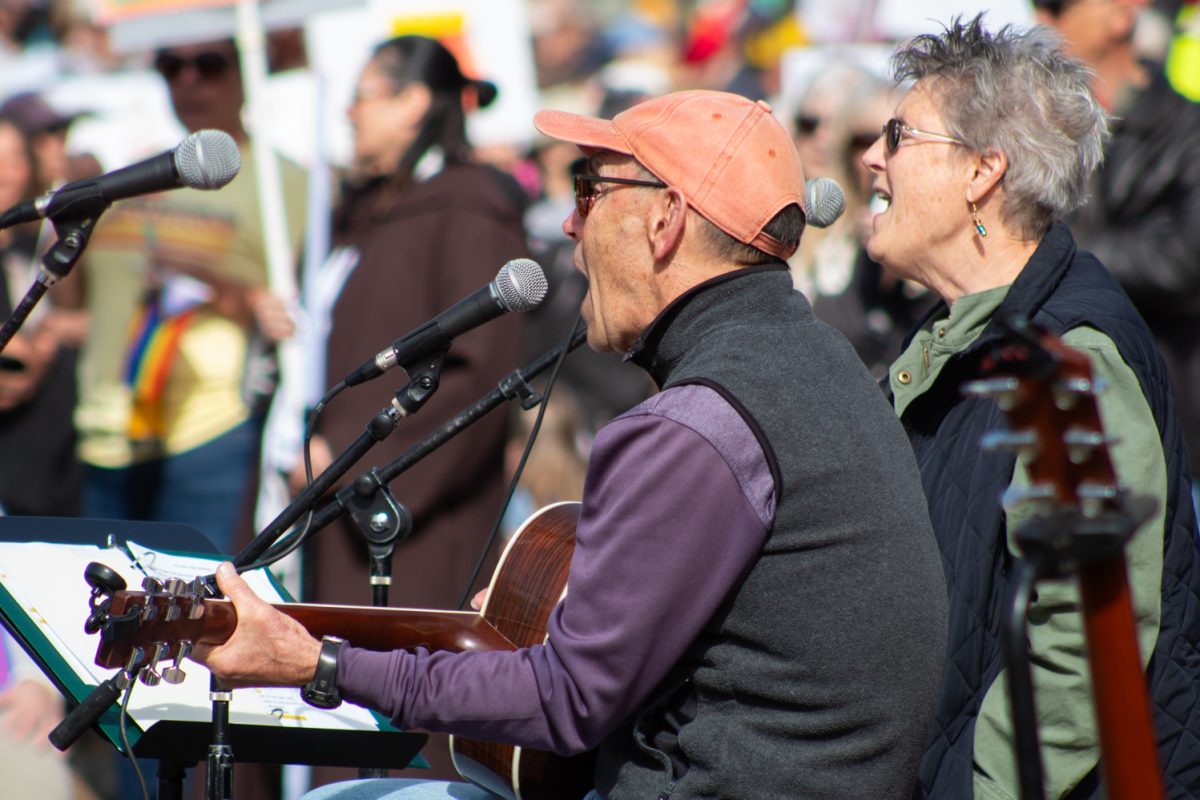 Frank Moore, a performing artist since 1973, sings an original song with a colleague to a crowd of No Kings attendees in Fort Collins’ Civic Center Park March 28. Moore performed this song, We are All in this Boat Together at the last No Kings rally in October of 2025. “Before I start, there really has, in America’s history, only been two kings. Elvis, and Arnold Palmer,” Moore said.
