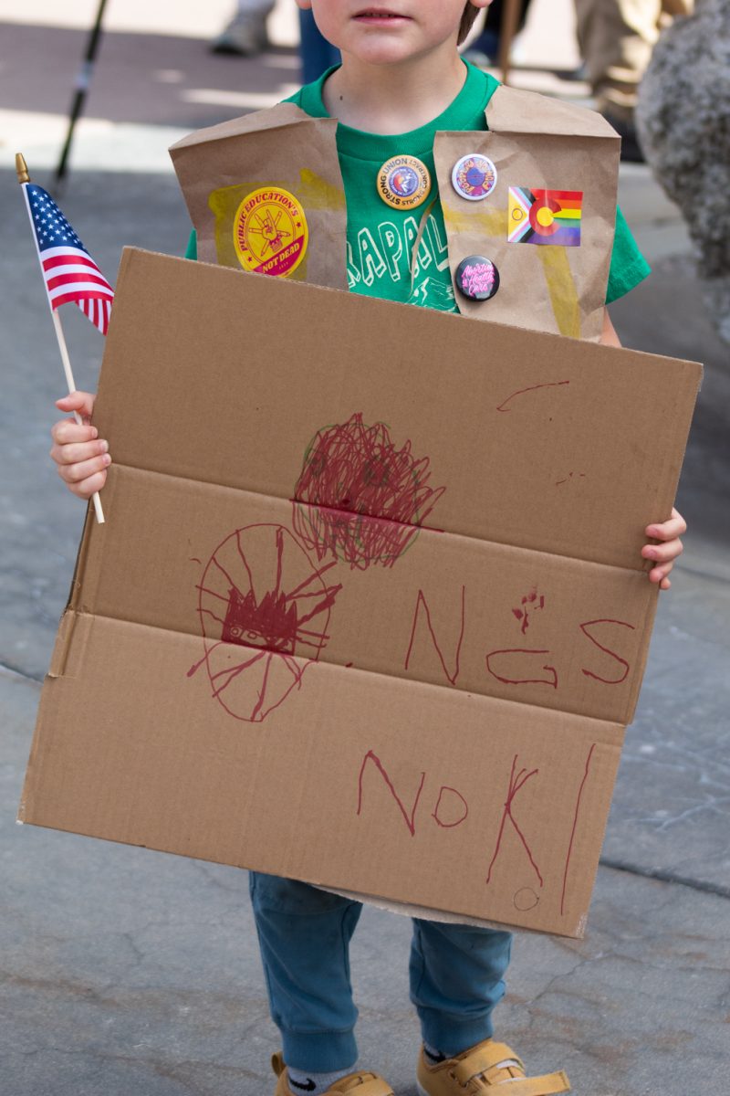 An anonymous young protester holds his handmade sign reading ‘No Kings’ and an American flag March 28. In addition, he wears a hand made paper vest with pins and stickers. This attendee was one of an estimated 10,000 who showed up to attend the No Kings protest, where people in cities across the country expressed their dissatisfaction with the Trump administration.