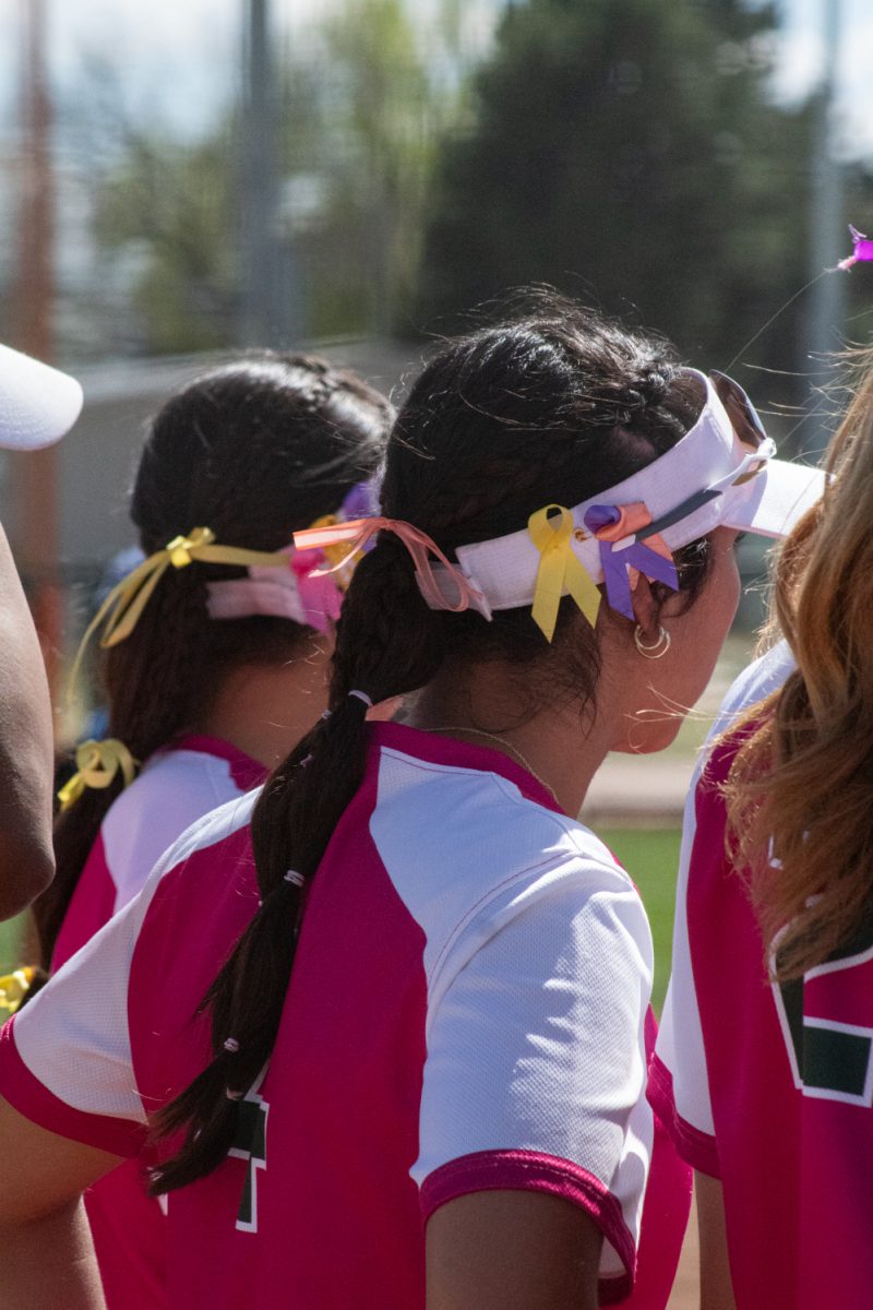 Freshman Jasmin Martinez listens to a team meeting during Colorado State University's Pink Out and Colors for a Cause game against Boise State at the CSU Softball Field Mar. 29. Her hat displays ribbons, which were also given out to spectators, to raise awareness for different cancers. The Rams won this game 7-6 in a walk-off win.