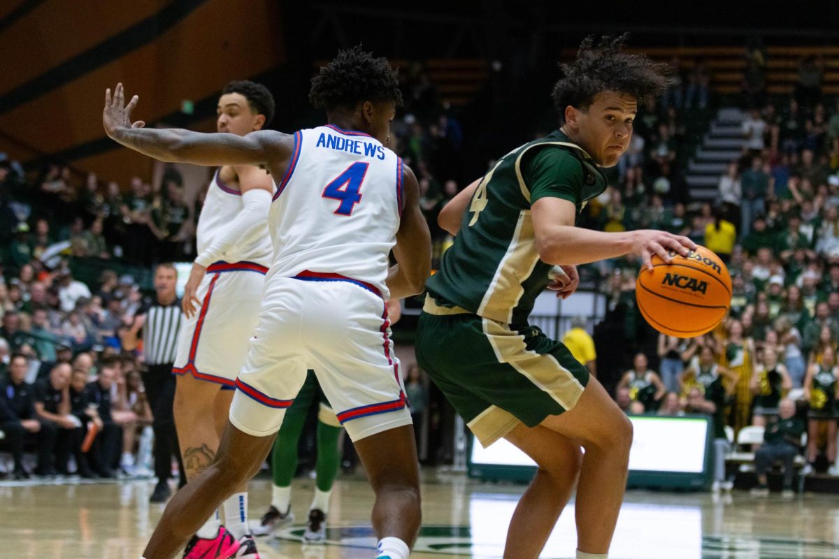 A man in an all green jersey with his back to a man in an all white jersey, holds the ball in his right hand as he runs by the other man.