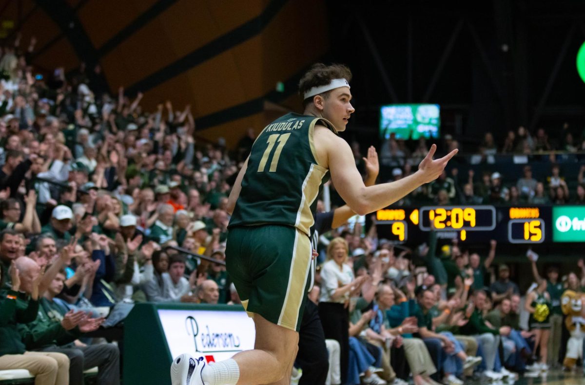 A man in an all green jersey extends his right hand in front of him gesturing a three pointer with his fingers.