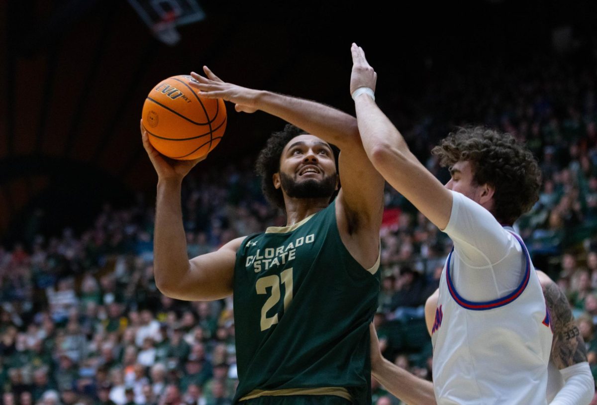 A man in an all green jersey faces away from a man in an all white jersey in front of him. The man in green has the ball above his head with both hands.