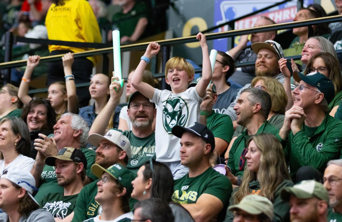 A child wearing a white shirt with the Colorado State University logo on it jumps with his hands in the air.