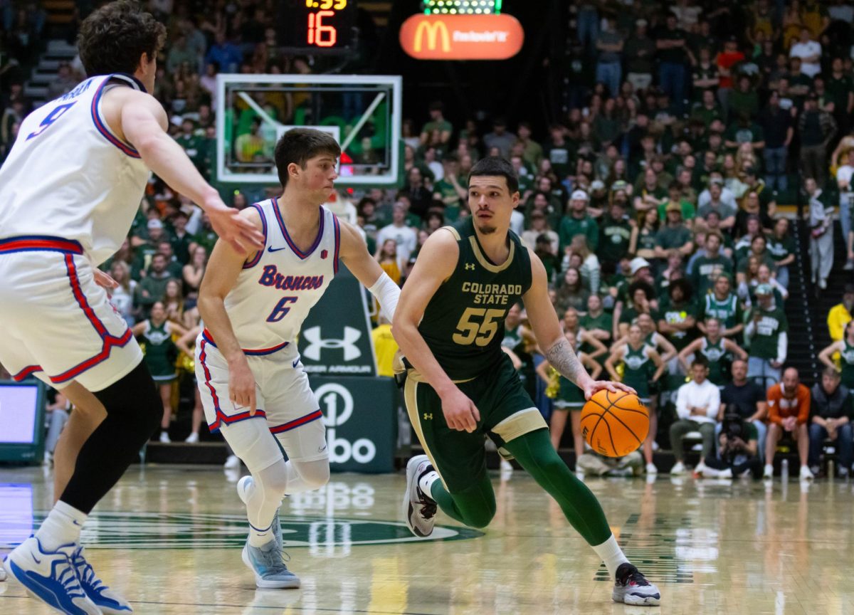 A man in an all green jersey runs around two men wearing all white jerseys, the man in green has the ball in his left hand.