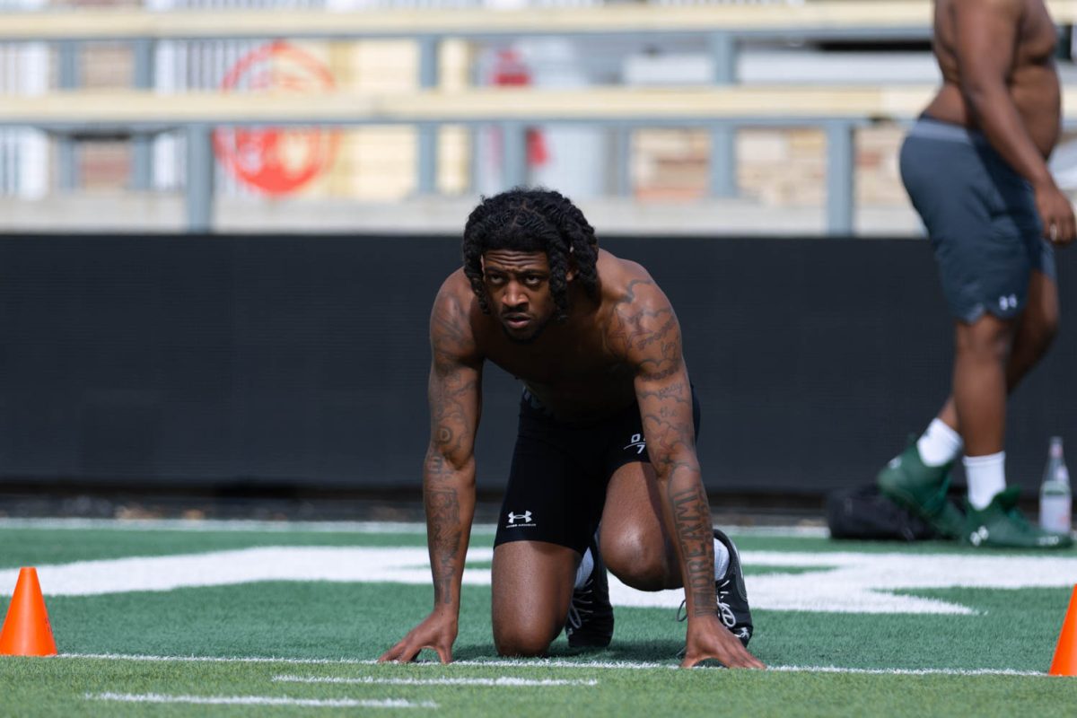 A man wearing black compression shorts crouches down in front of two cones, he looks forward.