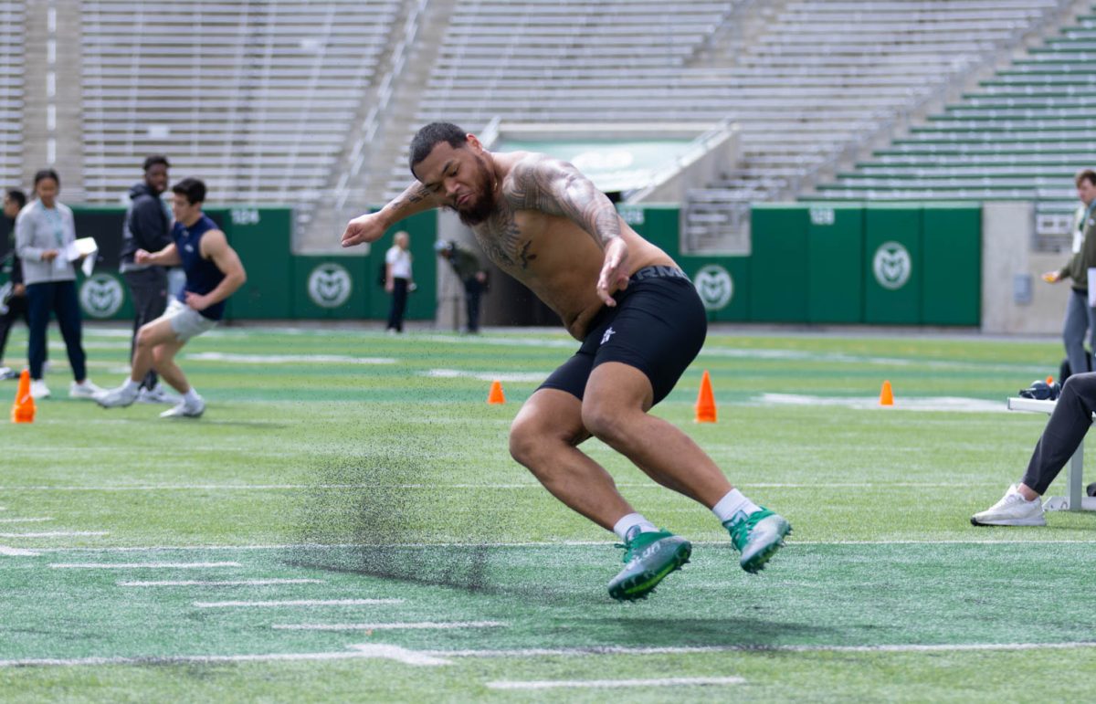 A man in black compression shorts jumps in front of him to touch the turf. Black specs from the turf fly behind him.