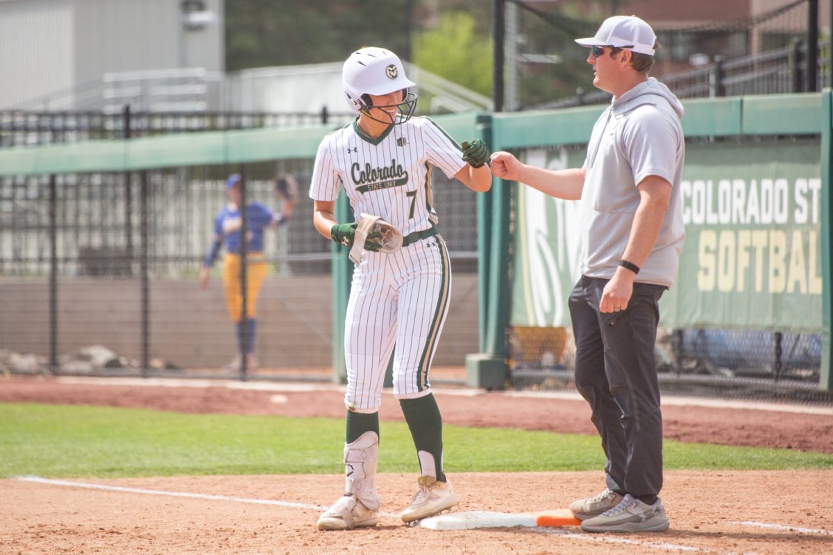A woman in softball uniform fist bumps a man.