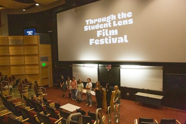 Eight people, men and women, stand in front of a screen that reads, “Through the Student Lens Film Festival."