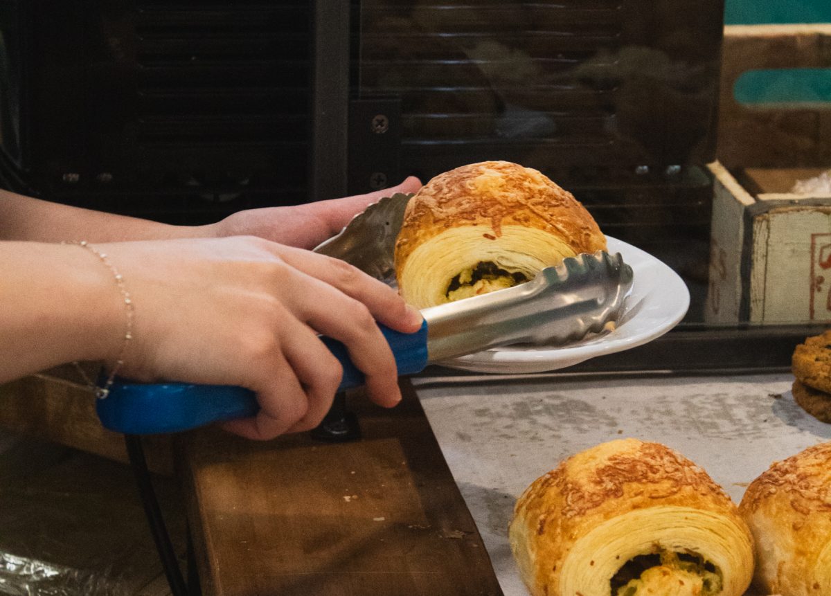 A barista at Trickster Bakery &amp; Cafe uses tongs to place a pastry on a plate Aug. 20.  The business, co-owned by Jenn Lewis and Shannon Morr, supports the local economy by partnering with local vendors and donates leftover pastries to the UC Health Family Medicine Center food pantry. “I’m mostly proud of kind of the vibe we’re cultivating. Obviously the pastries too, but those I knew would be good, like, from the beginning,” Morr said.