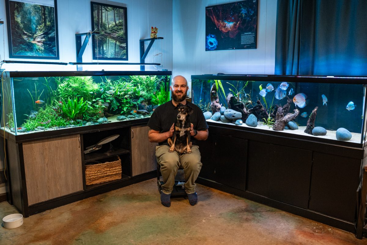 Michael Amato and his dog Mollie pose in between his 125-gallon Boesemani Rainbow community tank and 125-gallon discus tank Oct. 13. 